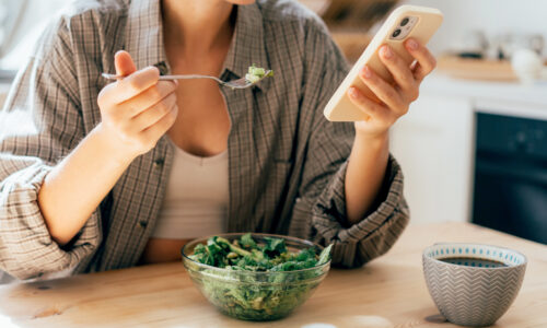 Modern woman having breakfast while using mobile phone